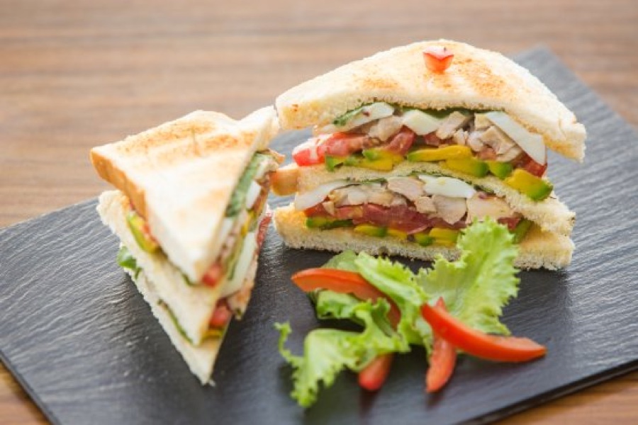 Accra Chicken Club sandwich with vegetables on a black plate